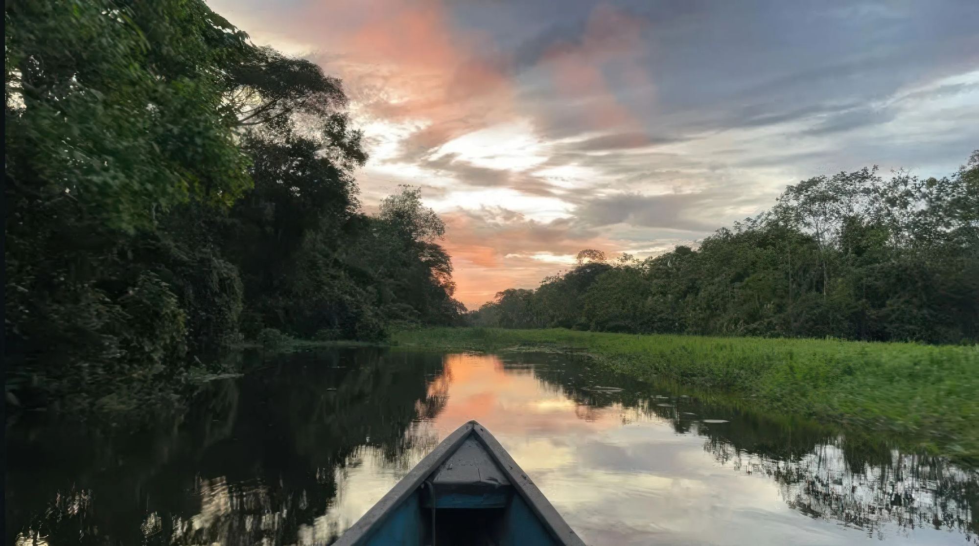 Le ciel rose du soir se reflète sur l'eau immobile, vu depuis l'avant du bateau