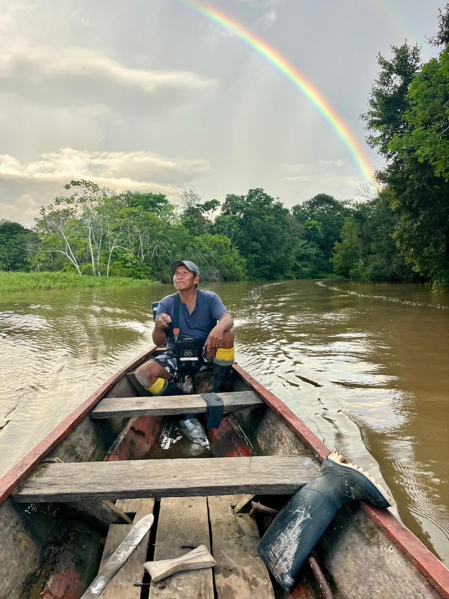 Un guide de la communauté seul dans sa pirogue, sous un arc-en-ciel