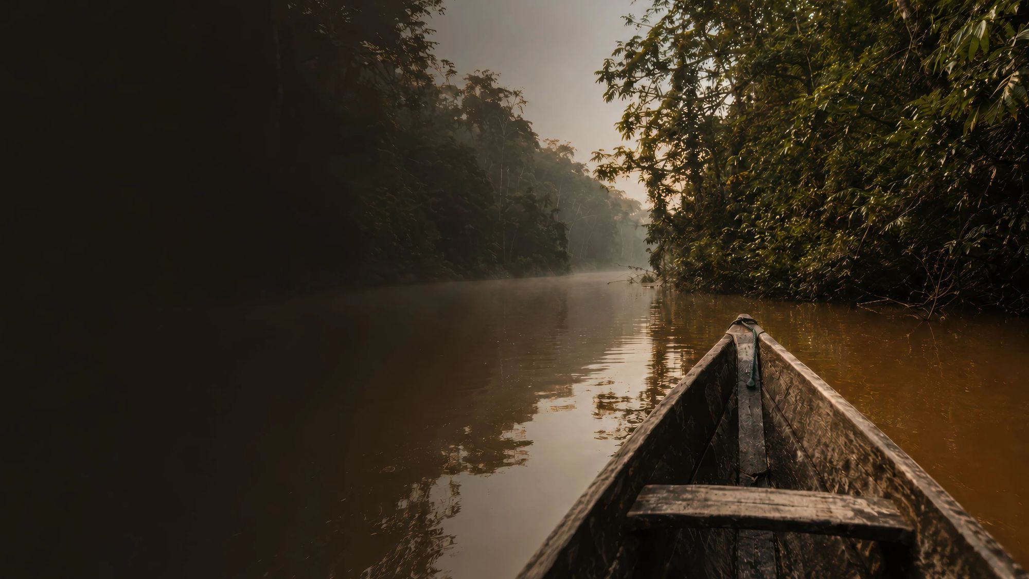 La proa de un bote de madera avanza por el río entre la niebla de la mañana